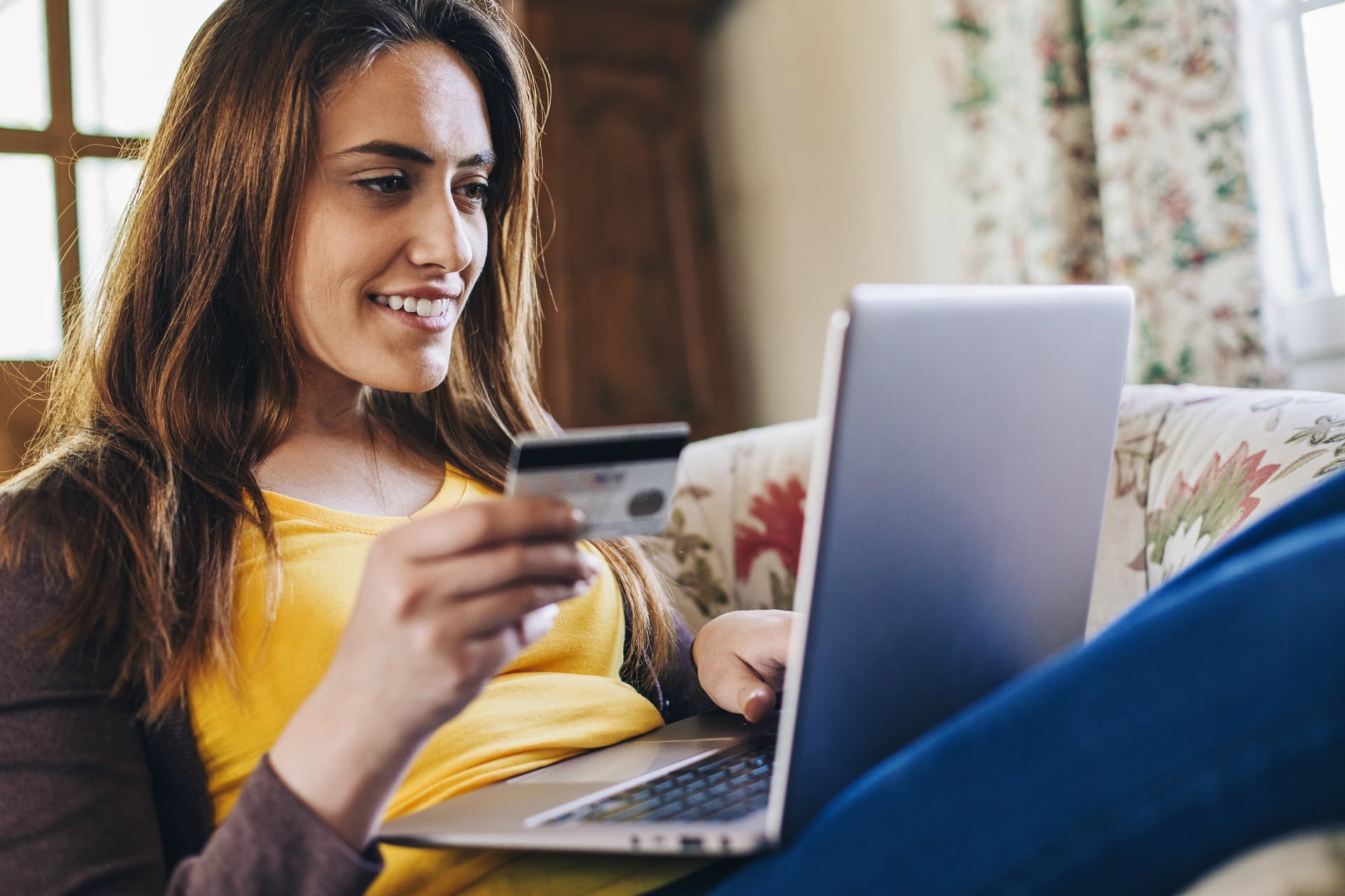 Mulher em casa segurando um cartão de crédito enquanto usa um notebook | Entrevista: SEO para E-commerce